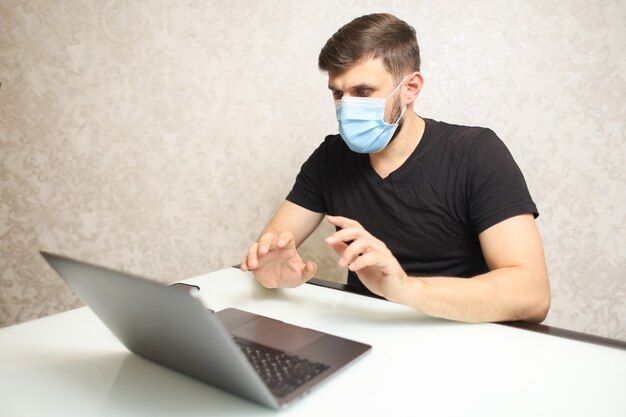 a man in a medical mask on selfisolation works at a laptop