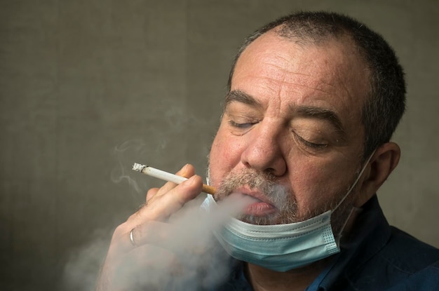 Foto un uomo con una maschera medica fuma una sigaretta