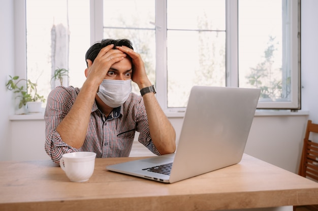 Man in medical mask using laptop at home