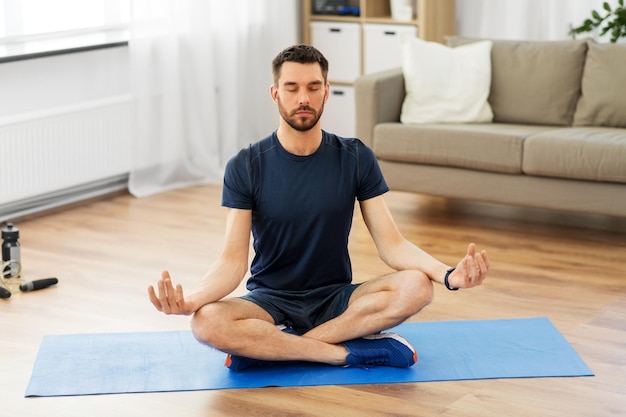 man meditating in lotus pose on yoga mat at home