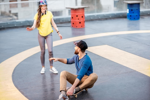 Man meeting his girlfriend sitting on the skateboard outdoors on the rooftop playground