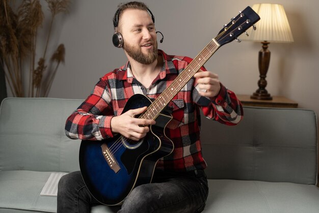 Man met akoestische gitaar zit op de bank met koptelefoon blanke gitarist die oefent op een muziekinstrument