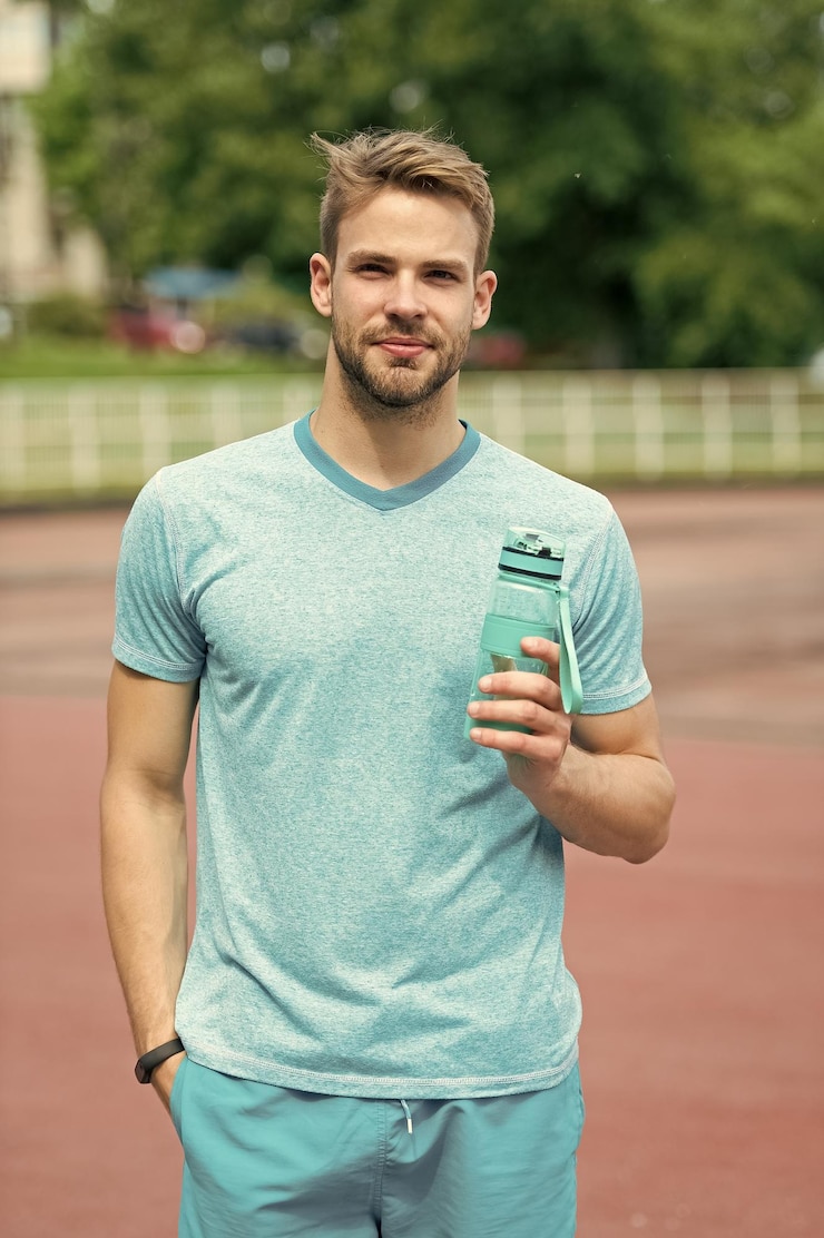 Foto man met atletisch uiterlijk houdt fles met water vast atleet drinkt water na training in stadion op zonnige dag man atleet in sportieve kleding traint buiten sport en gezond levensstijlconcept