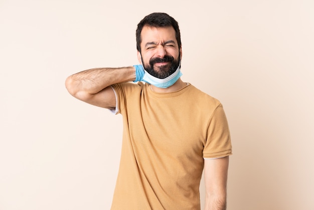 Man met baard beschermen tegen het coronavirus met een masker en handschoenen over geïsoleerde muur met nekpijn