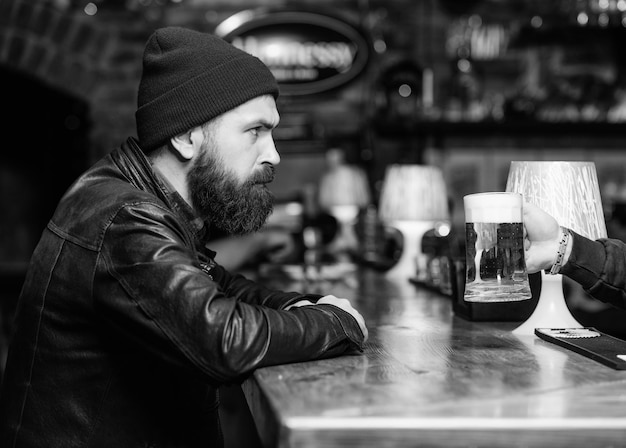 Man met baard brengt vrije tijd door in donkere bar Brutale eenzame hipster Hipster ontspannen aan bar Brutale hipster bebaarde man zit aan bar vrijdagavond Bar is ontspannende plek om te drinken en te ontspannen