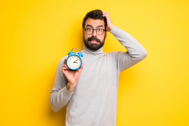 Man met baard en coltrui rusteloos omdat het te laat is geworden en met een vintage wekker