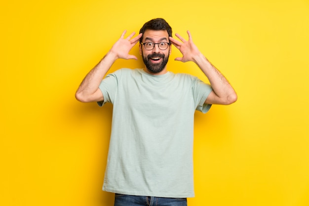 Man met baard en groen shirt met verrassing en geschokte gelaatsuitdrukking