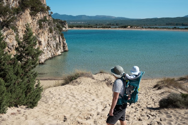 Man met baby in rugzak wandelen op een prachtige plek blauw zeezand strandzeegezicht