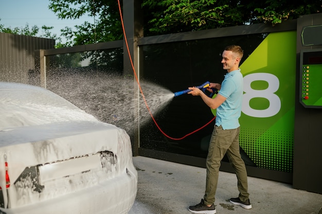 Man met behulp van hogedruk waterpistool met schuim, hand car wash station. Autowasindustrie of bedrijf. Mannelijke persoon reinigt zijn voertuig van vuil buitenshuis