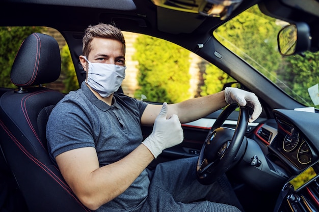 Man met beschermend masker en handschoenen autorijden. epidemie. blijf veilig door duimen omhoog te laten zien.