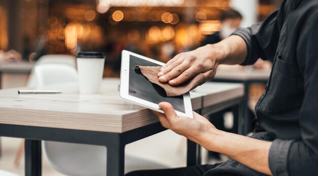 Man met beschermend masker veegt het scherm van een digitale tablet af met ontsmettingsmiddel