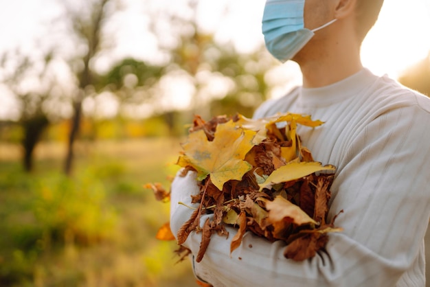 Man met beschermend medisch masker maakt herfstbladeren schoon in het park Man in handschoenen verzamelt