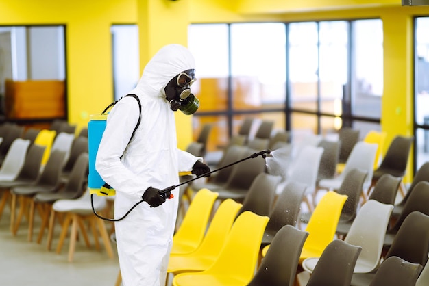 Man met beschermend pak die de aula desinfecteert met chemische spray om coronavirus te voorkomen