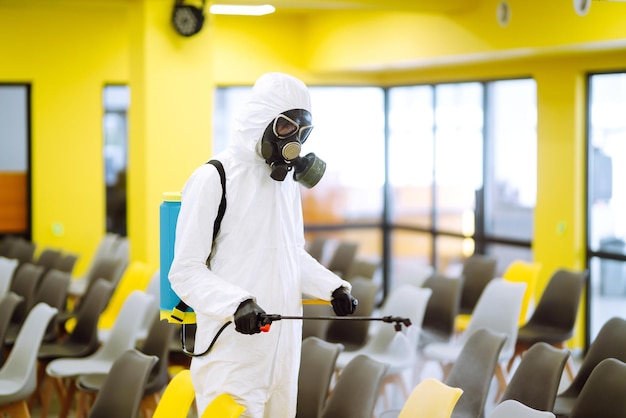 Man met beschermend pak die de aula desinfecteert met chemische spray om coronavirus te voorkomen