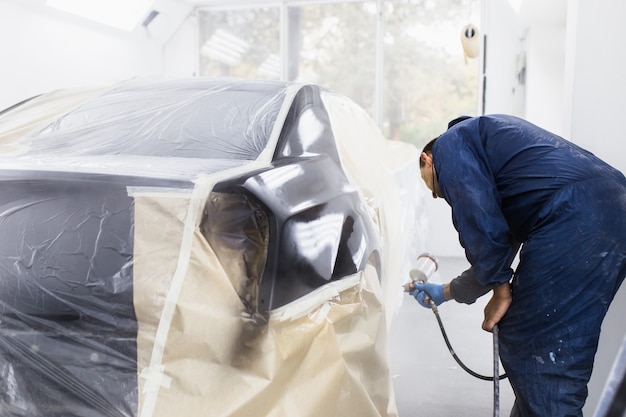 Man met beschermende kleding en masker schilderij auto met behulp van spray compressor. Selectieve aandacht.