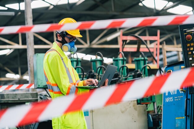 Foto man met beschermende werkkleding die een laptop gebruikt in de fabriek