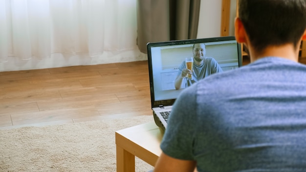 Man met bier in een videogesprek met een van zijn vrienden tijdens wereldwijde isolatie.