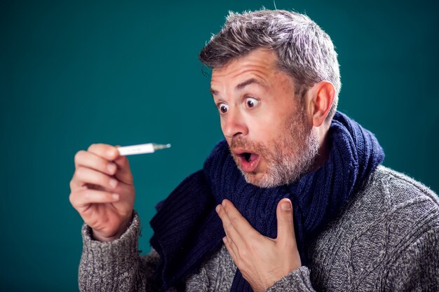 Man met blauwe sjaal kreeg de griep en meet de temperatuur. Mensen, gezondheidszorg en geneeskundeconcept