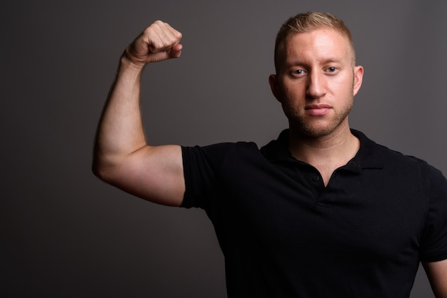 Foto man met blond haar dragen zwarte poloshirt op grijze muur