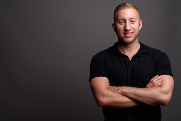 Man met blond haar dragen zwarte poloshirt op grijze muur