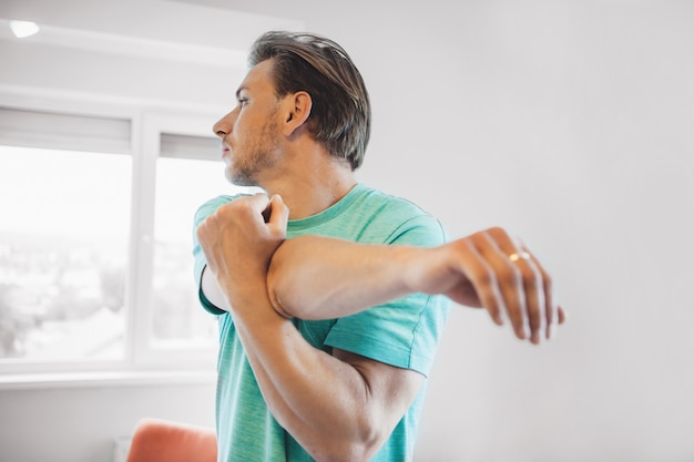 Man met blond haar en borstelharen opwarmen voordat hij thuis yoga doet