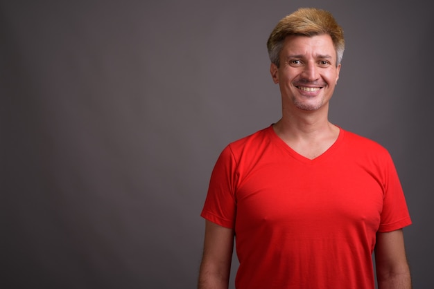 Man met blond haar, gekleed in een rood shirt tegen een grijze muur