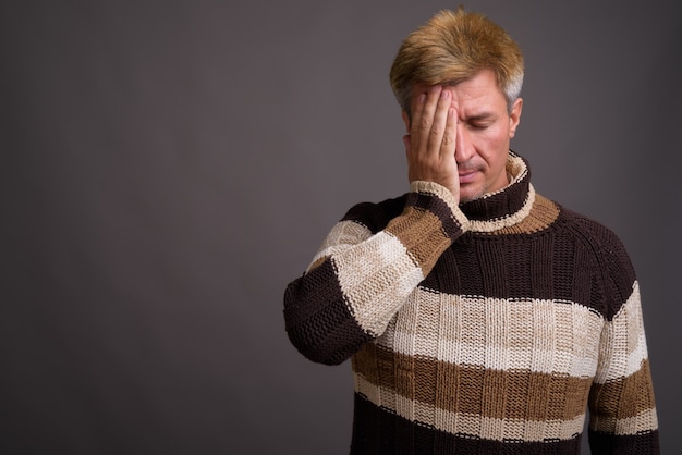 Man met blond haar met coltrui geïsoleerd tegen grijze muur