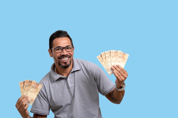 Man met Braziliaans geld glimlachend kijkt naar camera reclame concept geïsoleerd op blauwe achtergrond