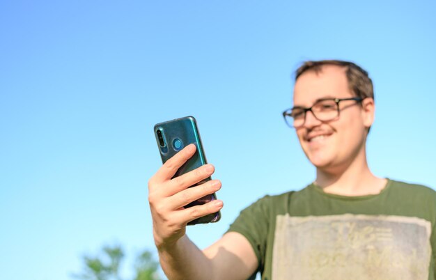 Man met bril en groene t-shirt op videogesprek vanaf zijn mobiele telefoon in het park