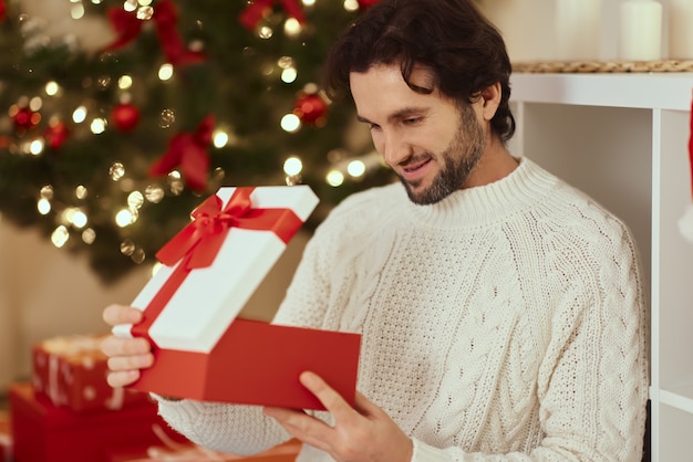 Man met cadeau in de geschenkdoos bij de kerstboom thuis