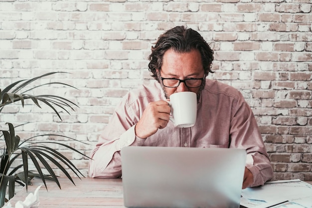 Man met computer aan de balie in thuiskantoor werkplek jonge volwassen blanke mensen op zoek naar laptop display en koffie drinken online slimme baan zakelijke activiteit moderne draadloze technologie