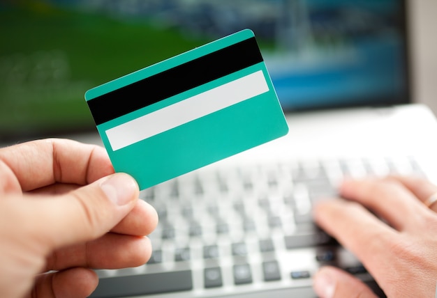 Man met creditcard in de hand en beveiligingscode invoeren met laptop toetsenbord