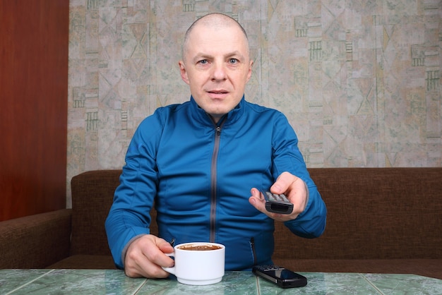 Man met de afstandsbediening voor de tv in de hand, koffie drinken