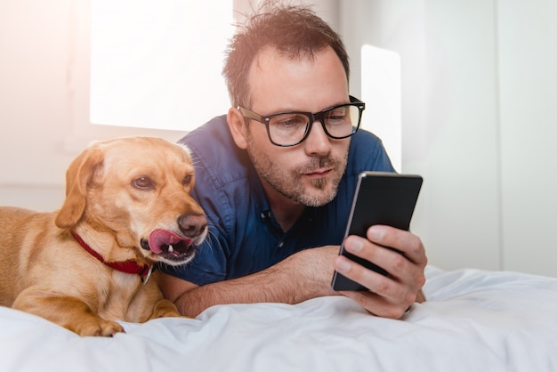 Man met de hond met behulp van slimme telefoon op het bed