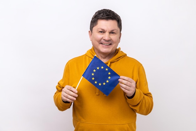 Man met donker haar die lacht en de EU-vlag vasthoudt en naar de camera kijkt met een brede glimlach