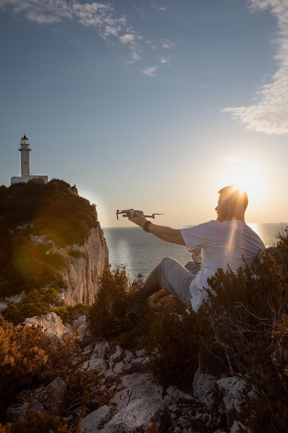 Man met drone op de klif in de buurt van zee zonsondergang boven de vuurtoren Lefkada Griekenland