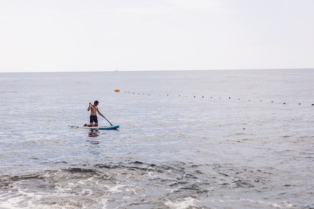 Man met een baard zwemt op stand-up paddleboard op een rustige blauwe oceaan. Supsurfen in het water