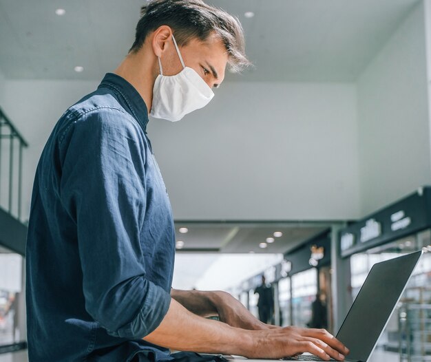 Man met een beschermend masker werkt op een laptop in een winkelcentrumgebouw