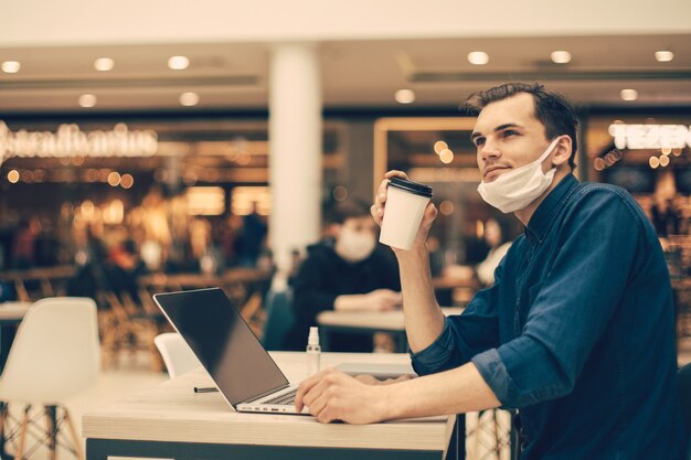 Man met een beschermend masker zit aan een tafel in een café. foto met een kopie-spatie