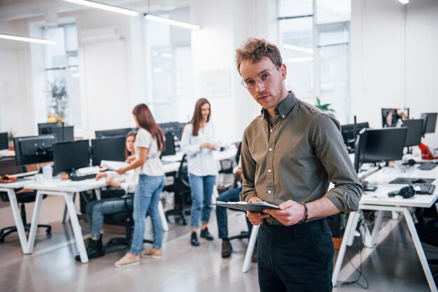 Man met een bril die voor zijn collega's op kantoor staat.