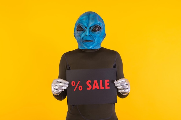 Foto man met een buitenaards masker met een blauw hoofd met een zwart bord met rode letters waarop staat 39 sale39 concept van bizar buitenaards grappig informatief raar en raar