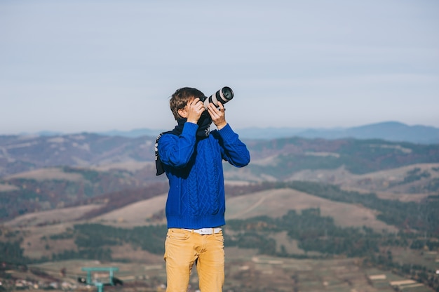 Man met een camera aan de rand van een klif met uitzicht op de bergen hieronder