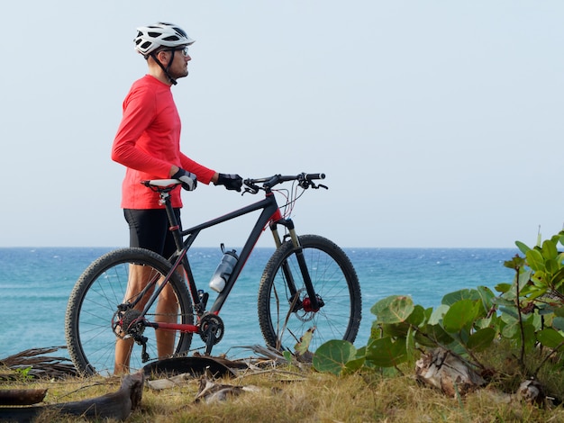 Man met een fiets staat op de oceaan kust