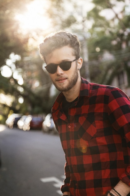 Man met een geruite shirt en een zonnebril terwijl hij op de weg staat