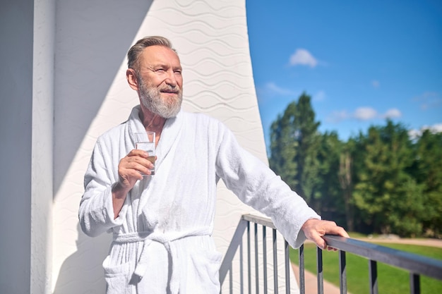 Man met een glas water op het balkon