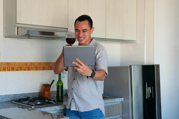 Man met een glas wijn die thuis een videogesprek voert met een tablet