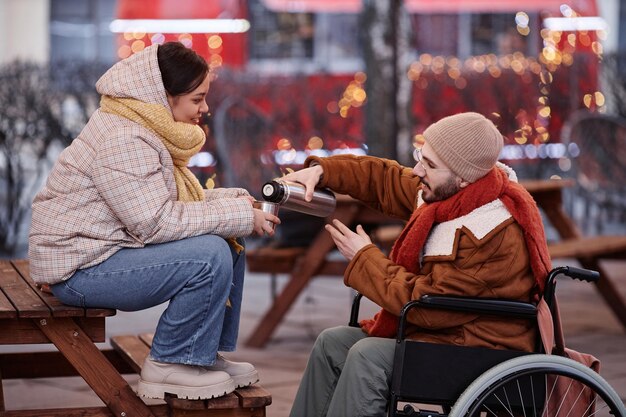 Man met een handicap die warme drankjes deelt met een jonge vrouw op een date in de winterstad