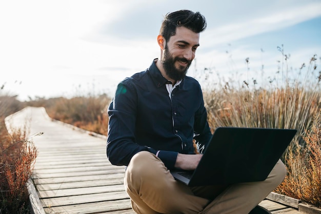 Man met een laptop terwijl hij op de promenade tegen de lucht zit