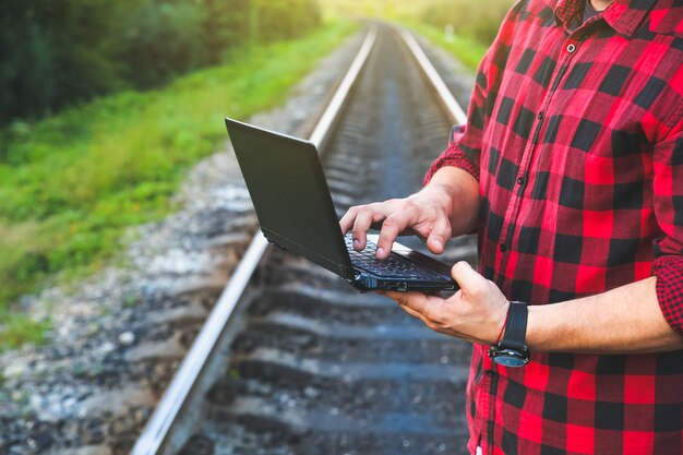 Man met een laptop zit op het spoor. Freelance hipster werknemer. De mens werkt op reis.