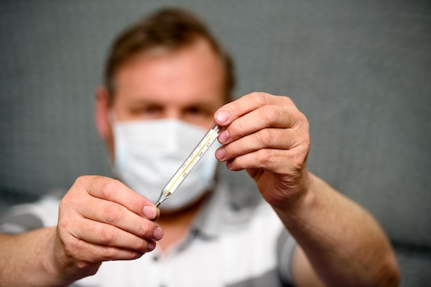 Man met een medisch masker houdt een thermometer in zijn handen een wazig plan van de close-up